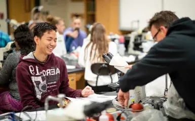 Male student in biology lab smiling by a microscope 