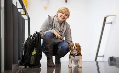 female student smiling and squatting next to a small service dog