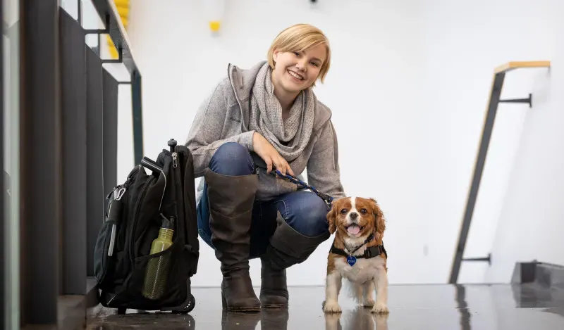 female student smiling and squatting next to a small service dog